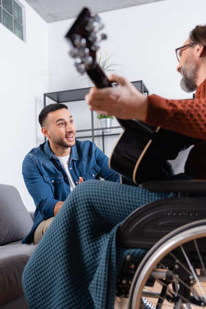 excited hispanic man near disabled father playing guitar on blurred foregroundの写真素材