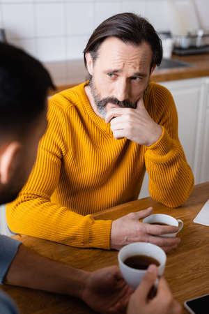 thoughtful man listening to son during conversation in kitchen, blurred foreground