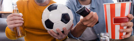 cropped view of father and son watching football match with beer and popcorn at home, banner