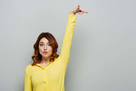 curly young woman pouting lips and pointing with finger isolated on grayの写真素材