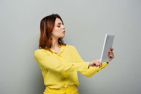 serious woman in yellow blouse using digital tablet with blank screen on grayの写真素材