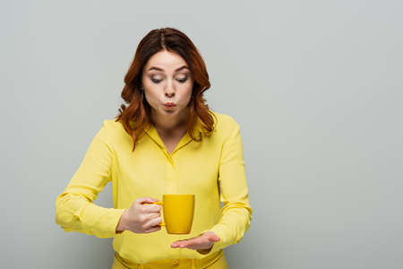 shocked woman in yellow blouse holding cup of hot tea on grayの写真素材