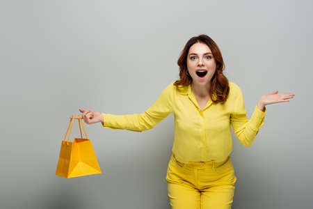 excited woman holding yellow shopping bag and pointing with hand on gray