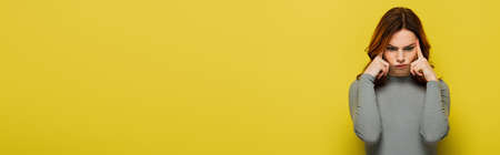 thoughtful woman in gray pullover touching head on yellow, banner