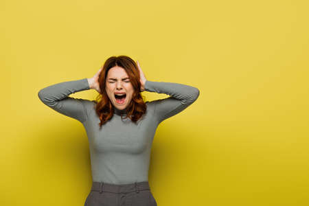 young woman screaming while touching head on yellowの写真素材