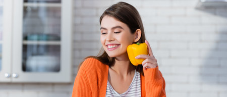 smiling woman holding fresh bell pepper in kitchen, bannerの写真素材
