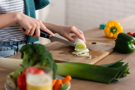 cropped view of woman cutting leek while preparing vegetable breakfast on blurred foregroundの写真素材