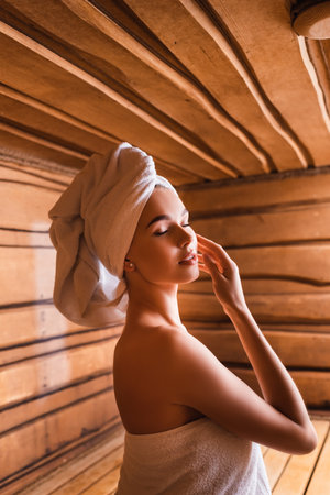 Young woman in white towels standing in saunaの写真素材