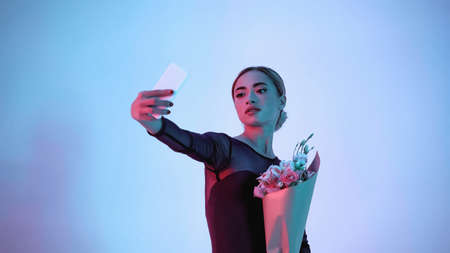 young ballerina holding flowers while taking selfie on blue
