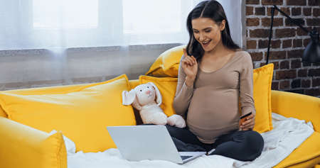 Smiling pregnant woman with credit card looking at laptopの写真素材