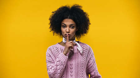 Young african american woman showing secret sign isolated on yellow