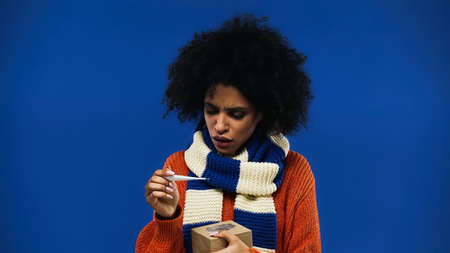 Ill african american woman holding thermometer and box isolated on blue