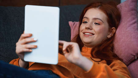 Smiling teenager using digital tablet on blurred foreground at homeの写真素材