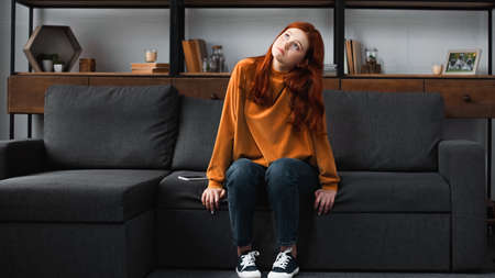 Pensive teen girl sitting on couch near smartphoneの写真素材