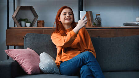 Smiling girl using smartphone near pillows on couchの写真素材
