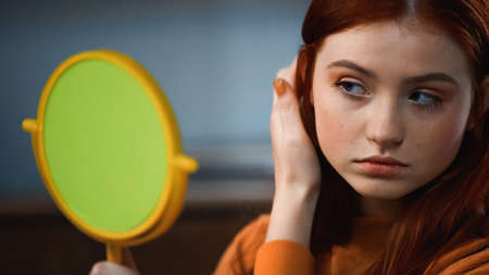 Red haired girl looking at mirror on blurred foregroundの写真素材