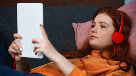 Teenager in headphones using digital tablet on blurred foreground
