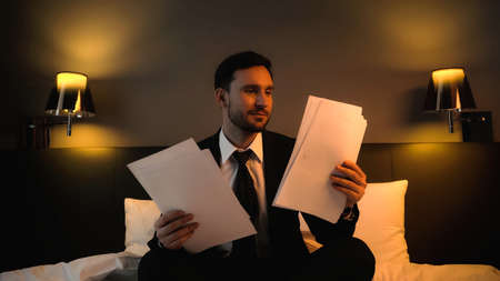 Bearded businessman looking at documents on hotel bedの写真素材