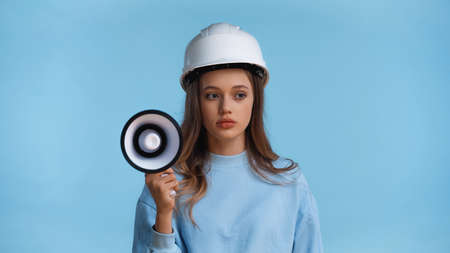 teenage girl in hard hat holding megaphone isolated on blueの写真素材