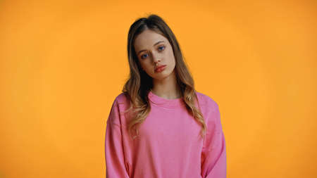 sad teenage girl in pink sweatshirt looking at camera isolated on yellowの写真素材