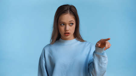 teenage girl in sweatshirt pointing with finger isolated on blue
