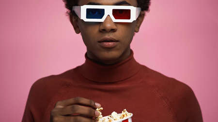 african american teenager in 3d glasses holding popcorn isolated on pink