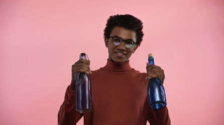 african american teenager in turtleneck sweater and eyeglasses looking at camera while holding...