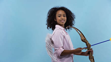 happy african american girl with wings holding crossbow isolated on blueの写真素材