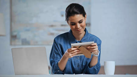 pleased woman holding photo frame near laptop on deskの写真素材
