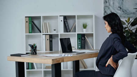 Side view of businesswoman suffering from back pain in office