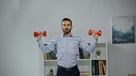 Businessman training with dumbbells in officeの写真素材