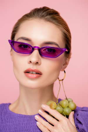 charming woman in purple eyeglasses, with fresh grapes earring isolated on pinkの写真素材