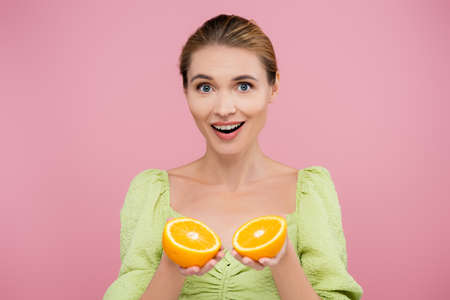 amazed woman holding halves of ripe fresh orange isolated on pink