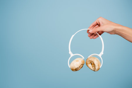 cropped view of woman holding headphones with mushrooms isolated on blueの写真素材