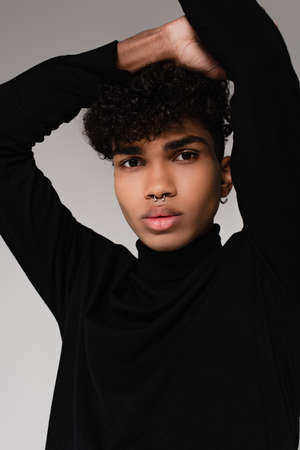 pierced african american man in black turtleneck sweater posing isolated on gray