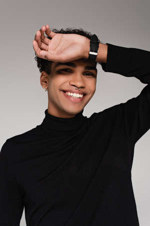 pierced african american man in turtleneck sweater smiling isolated on gray