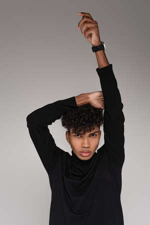 young african american man in turtleneck sweater with raised hands posing isolated on gray