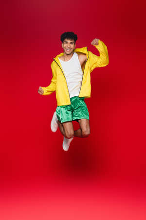 full length of smiling african american man in yellow jacket jumping on redの写真素材