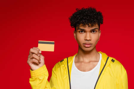 pierced african american man in jacket holding credit card isolated on redの写真素材