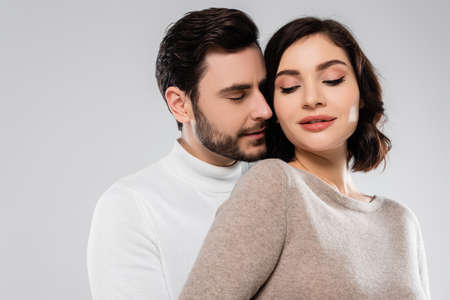 Young man with closed eyes standing near wife isolated on grayの写真素材