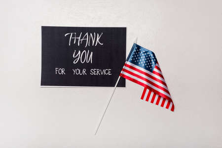 Top view of card with thank you for your service lettering and american flag on gray background