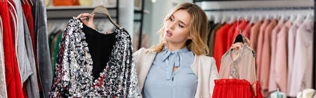 Young customer choosing dresses in showroom, bannerの写真素材