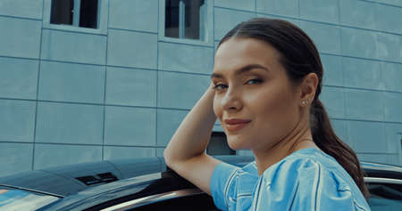 young woman looking at camera while leaning on car