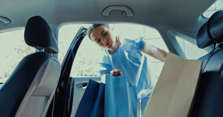young woman taking shopping bags from back seat of carの写真素材