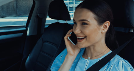 cheerful woman talking on smartphone inside of car
