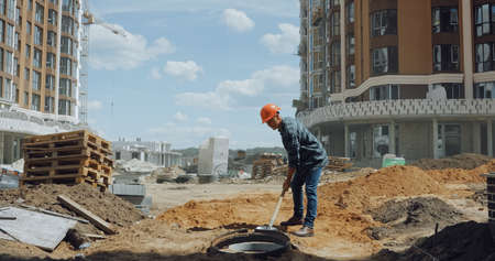 middle aged builder in hard hat digging ground with shovel on construction site