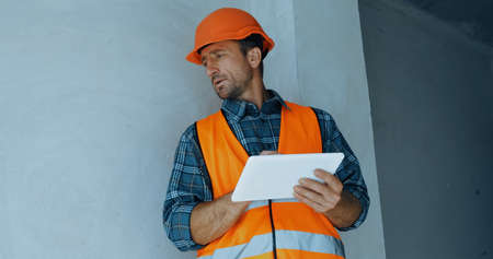 builder in safety helmet holding digital tablet on construction siteの写真素材