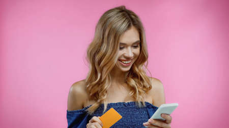 happy woman holding credit card and smartphone isolated on pinkの写真素材