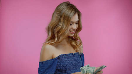 happy blonde woman counting dollars isolated on pink