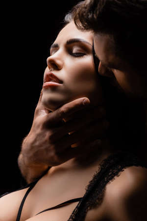 Young man touching chin of sexy woman with closed eyes isolated on blackの写真素材